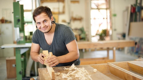  Ein junger Mann hobelt ein Stück Holz in der Werkstatt.