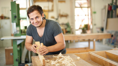 Ein junger Mann hobelt ein Stück Holz in der Werkstatt.