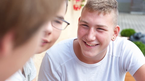 Nahaufnahme von einem Jugendlichen, der sich mit zwei anderen Personen unterhält.