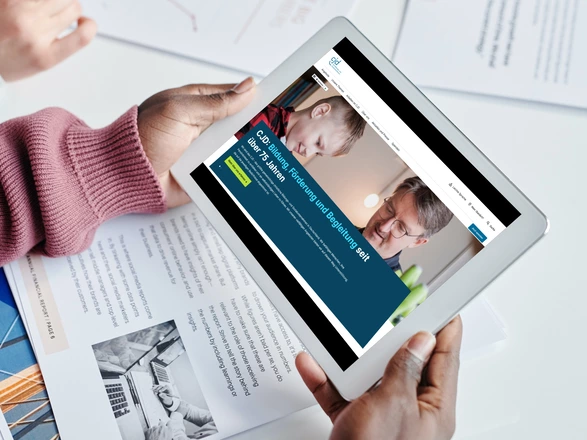 Zwei Hände halten ein Tablet. Auf dem Bildschirm ist die CJD Homepage zu sehen.