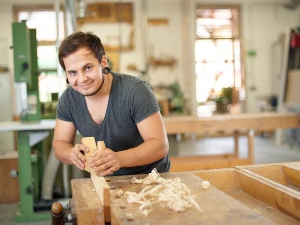  Ein junger Mann hobelt ein Stück Holz in der Werkstatt.